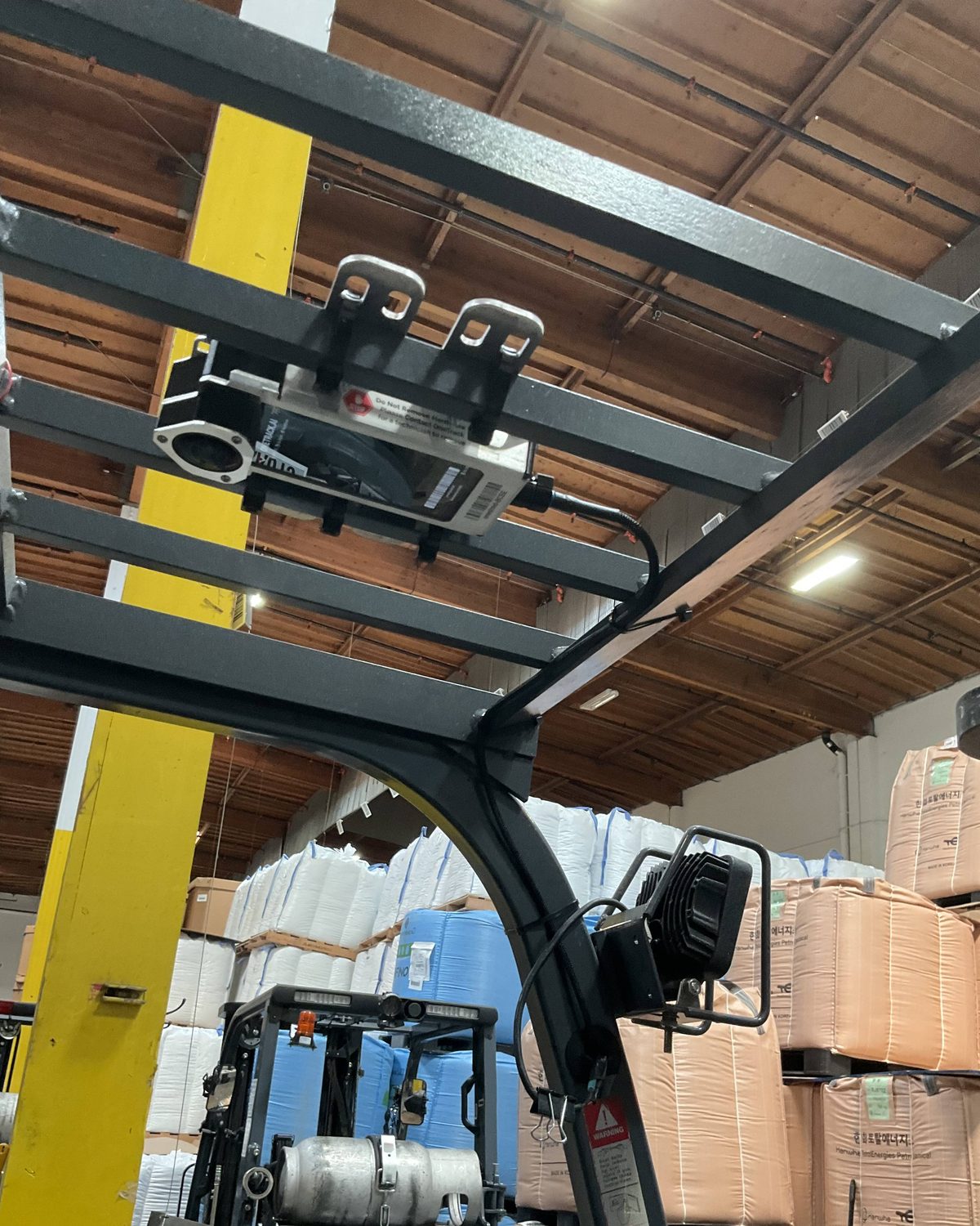 A OneTrack sensor mounted on the overhead guard of a sit-down forklift in a warehouse