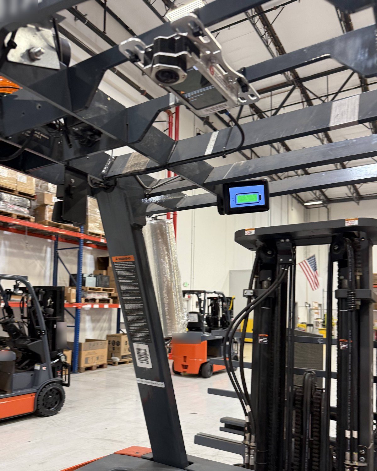 A OneTrack sensor on the overhead guard of a stand-up forklift, above the mast and the operator display