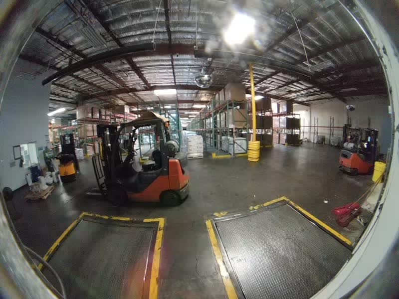 Dock door camera view across the dock floor, with dock plates in front and forklifts beyond