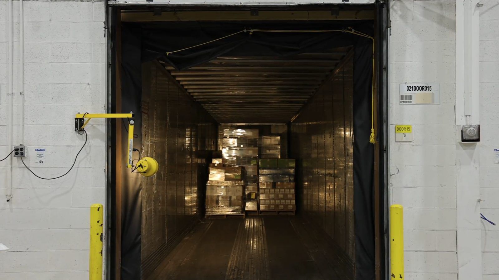 Load-facing camera view of an open trailer at a dock door, with loaded pallets at the far end