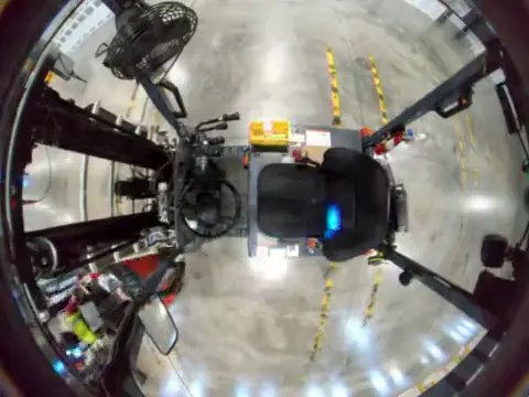 Overhead fisheye view looking down on a sit-down forklift's seat and controls, with the aisle all around