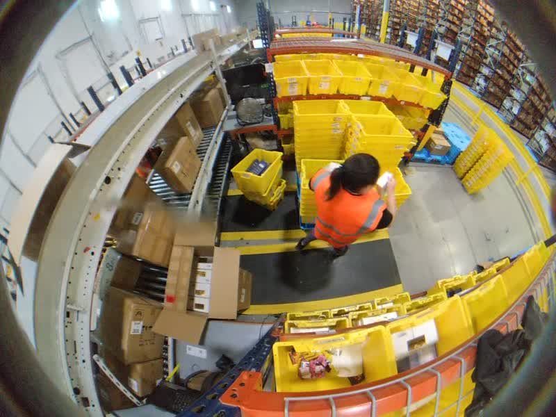 Static camera view from above a pack station, with totes, conveyors and boxes around a packer